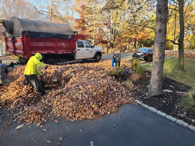 A dump truck is sitting on the side of the road next to a pile of leaves.