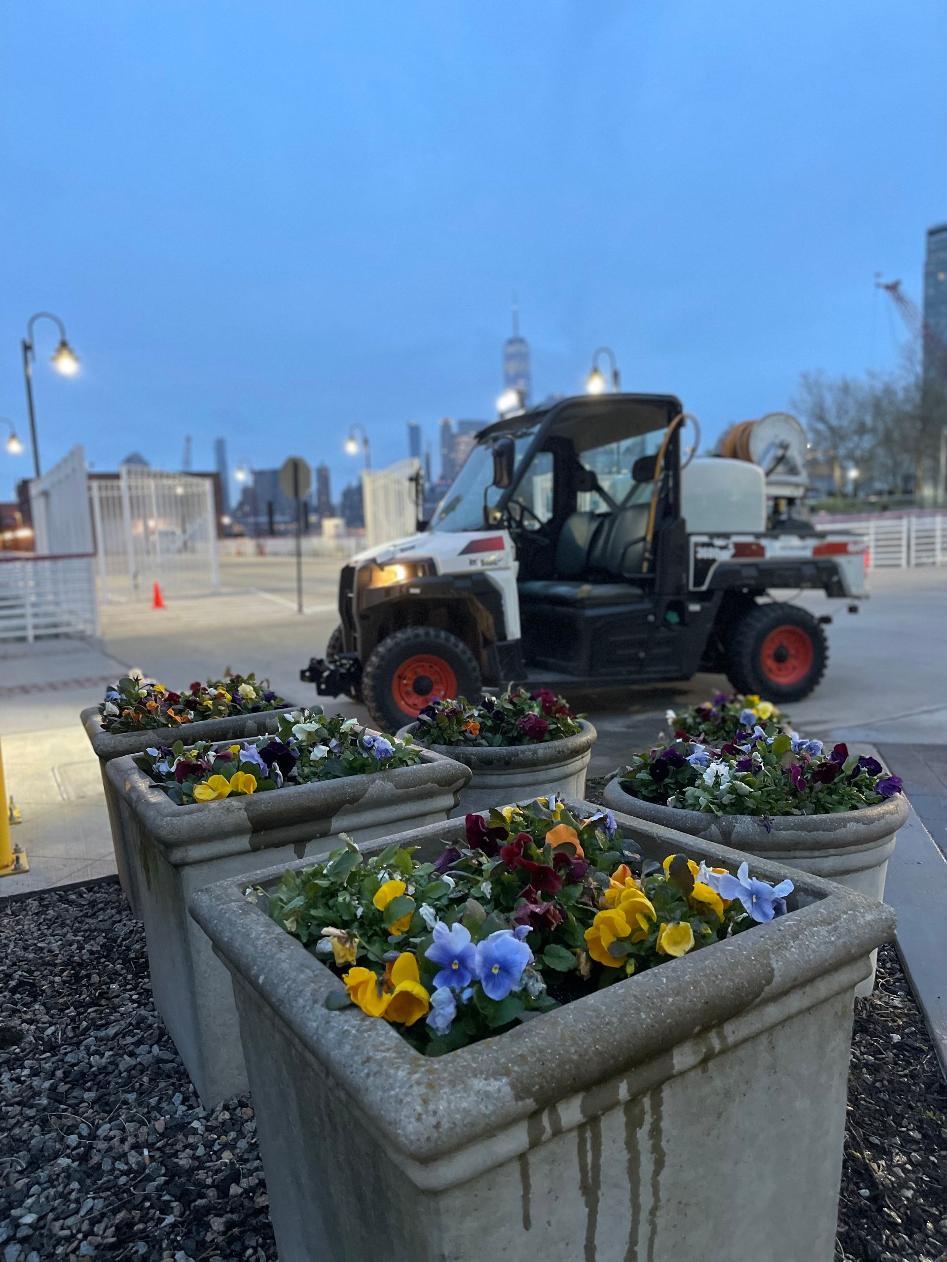 A white vehicle is parked next to a row of planters filled with flowers.