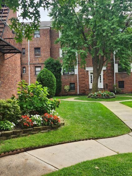 A brick apartment building with a lush green lawn and a sidewalk in front of it.