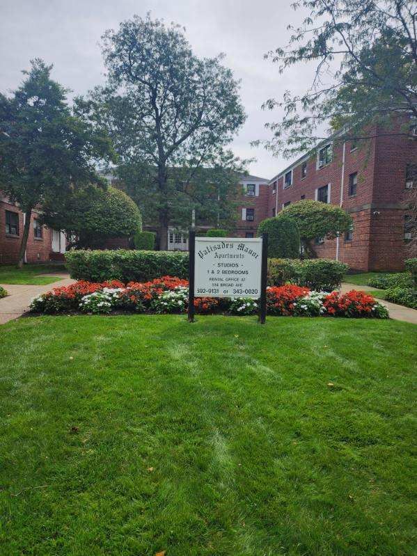 A sign in the middle of a lush green lawn in front of a brick building.