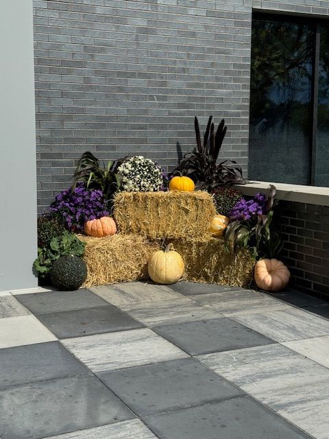 A bunch of pumpkins are sitting on top of hay bales on a patio.