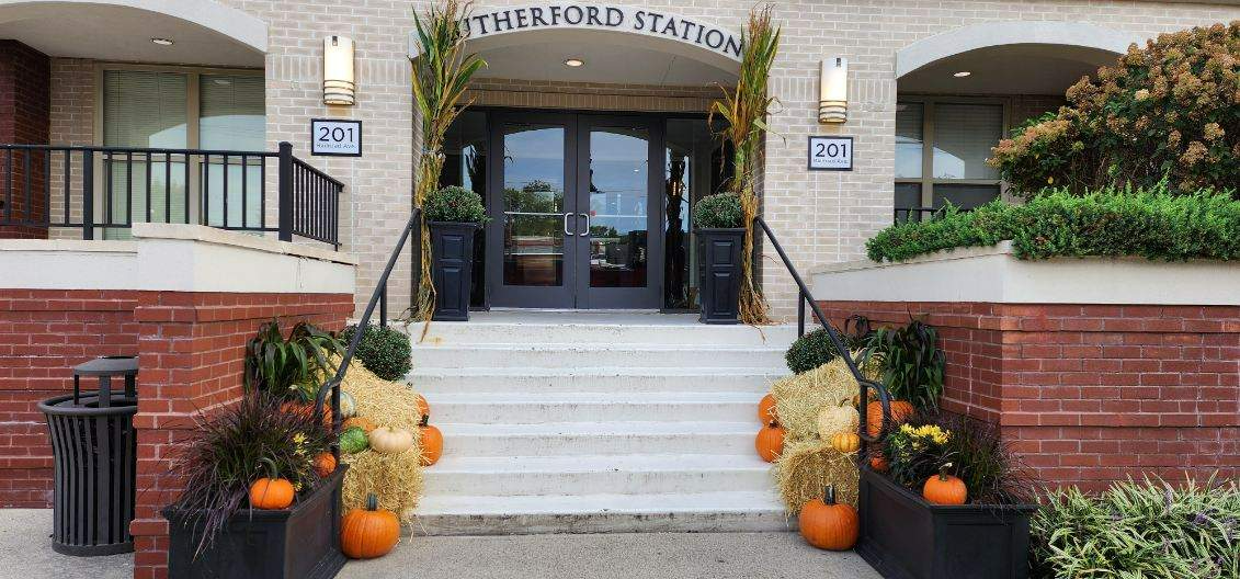The front entrance of a building decorated for Halloween with pumpkins and hay bales.