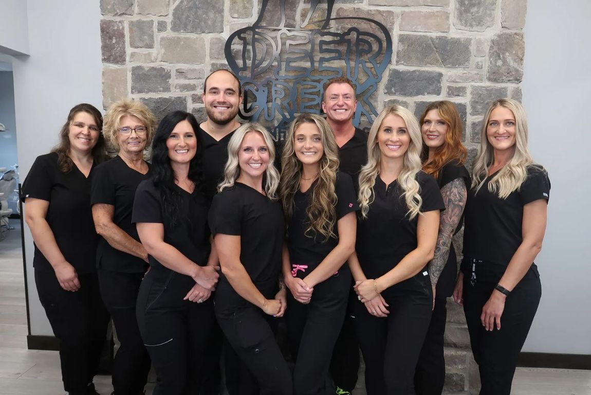 A group shot of the team of Deer Creek Dental Care employees in front of the business sign.