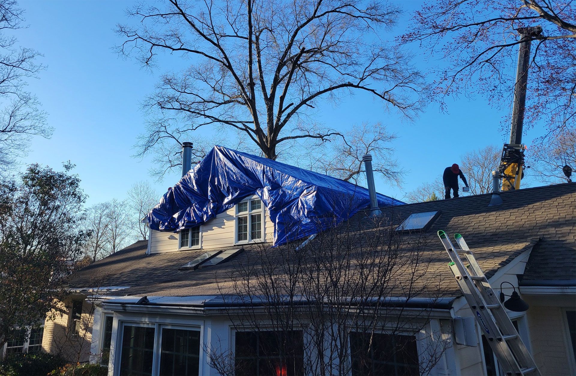 Roofer working on a house roof covered with blue tarp under a clear blue sky