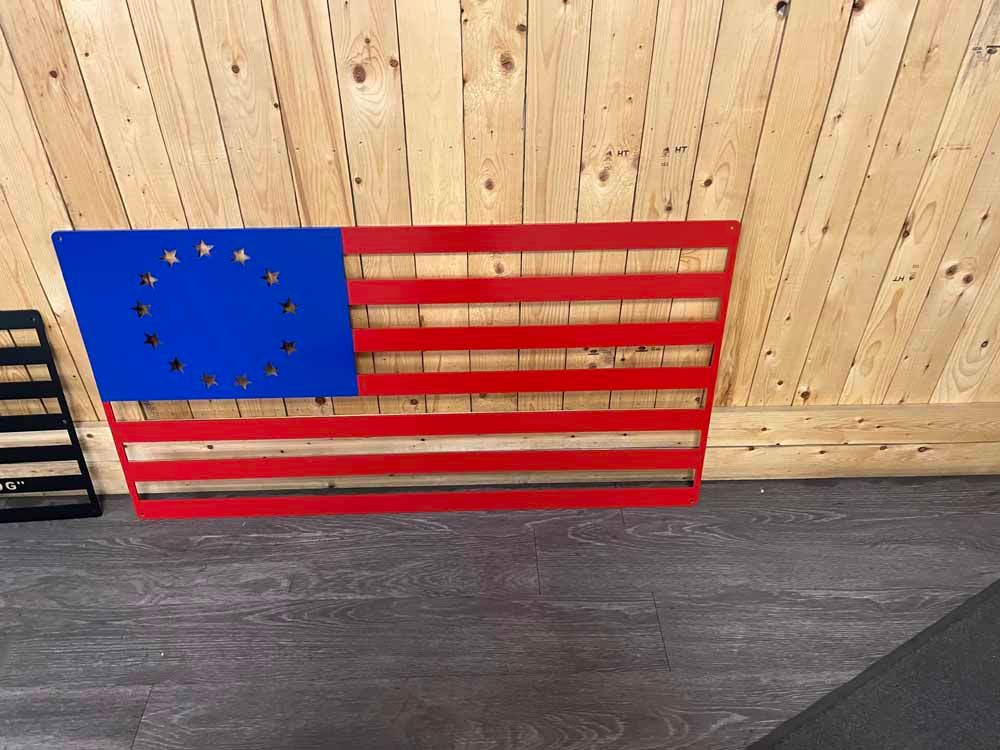 A red , white and blue american flag is hanging on a wooden wall.