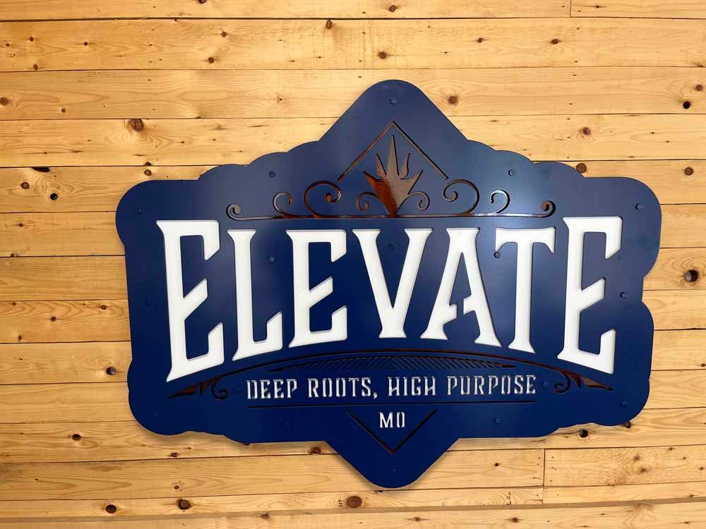 A blue sign on a wooden wall that says elevate