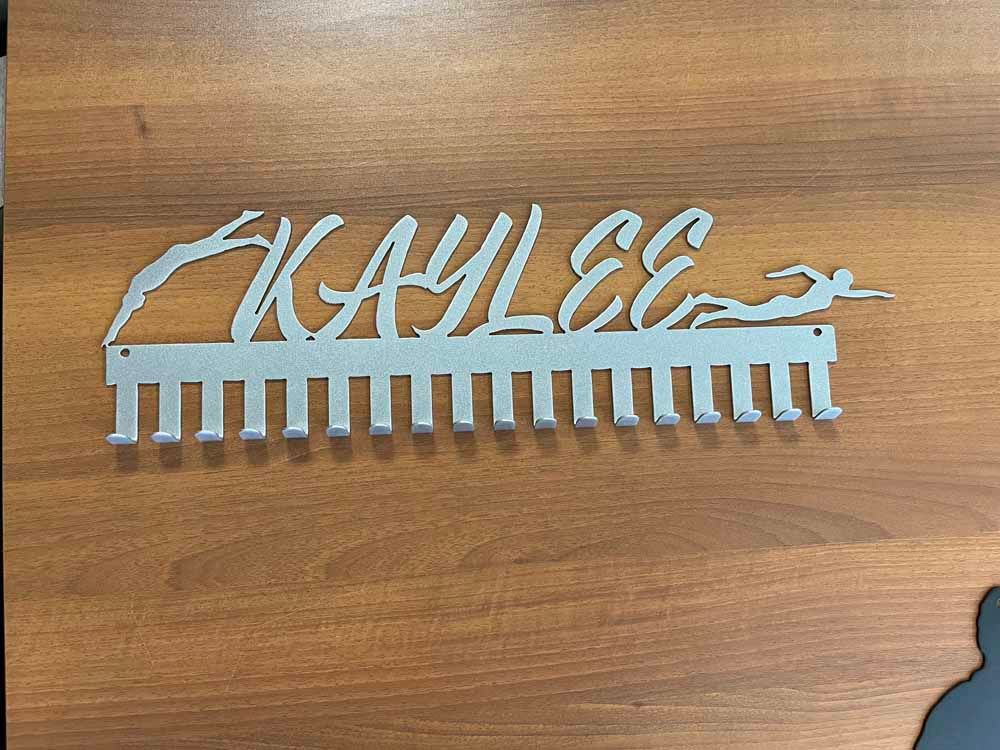 A medal holder with the name kaylee on it is sitting on a wooden table.