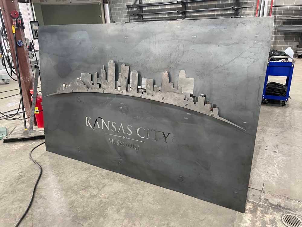 A large metal sign with a city skyline on it is sitting on the floor.