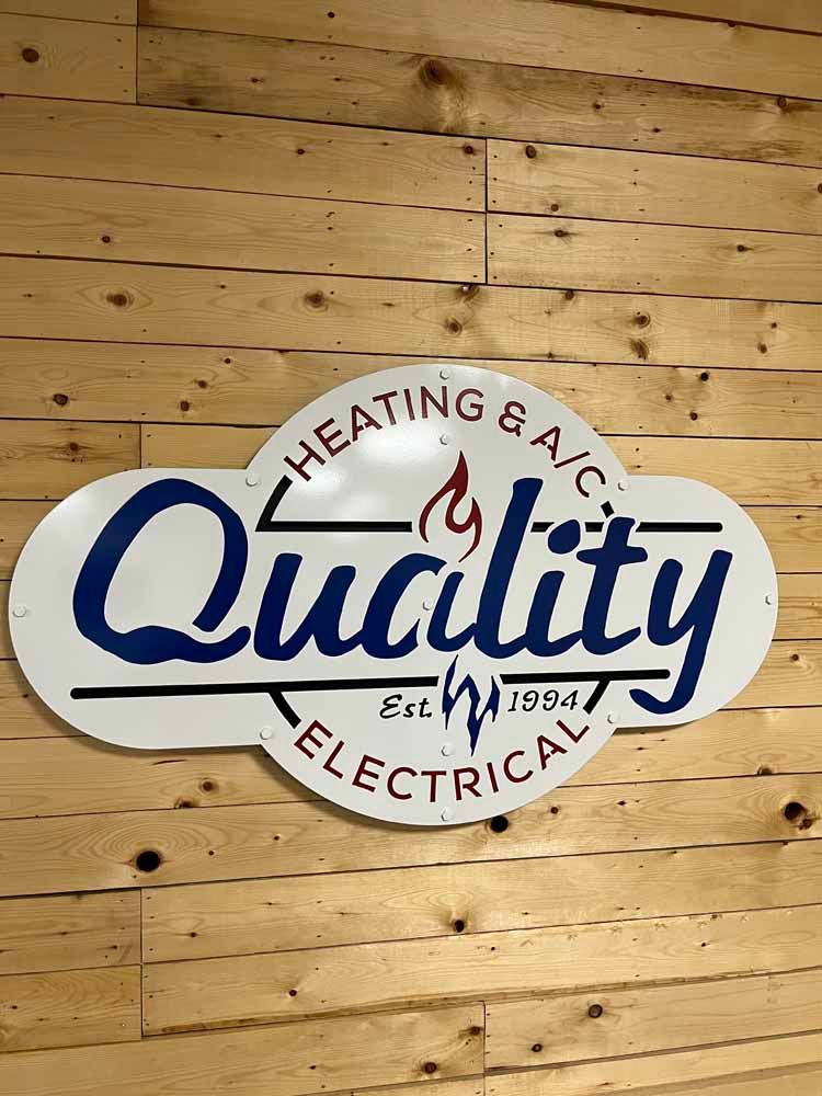 A quality electrical sign is hanging on a wooden wall.