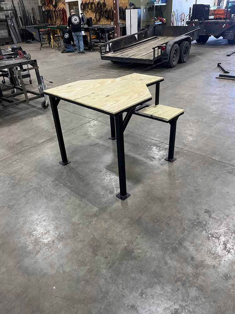 A wooden table is sitting in a warehouse next to a trailer.