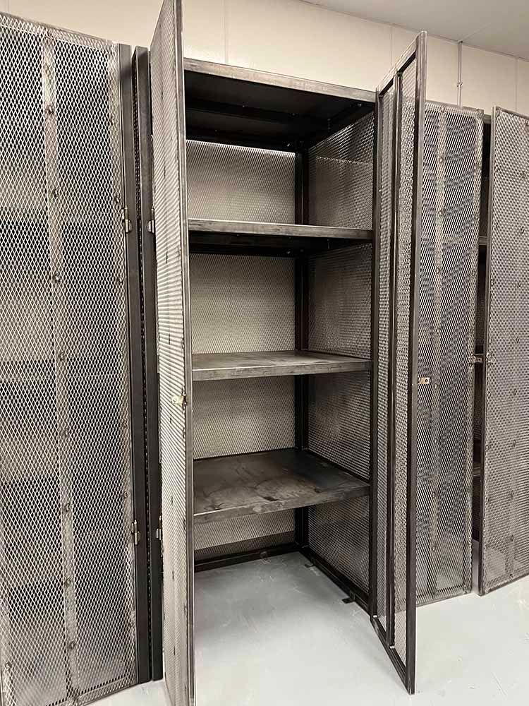 A metal cabinet with shelves and mesh doors is open in a room.