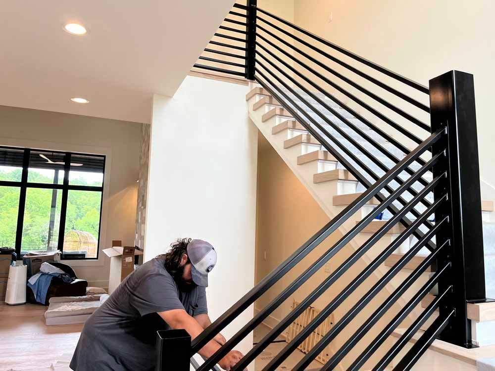 A man is working on a railing on a staircase in a house.