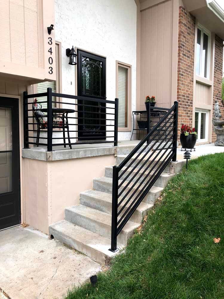 The front of a house with stairs and a black railing.