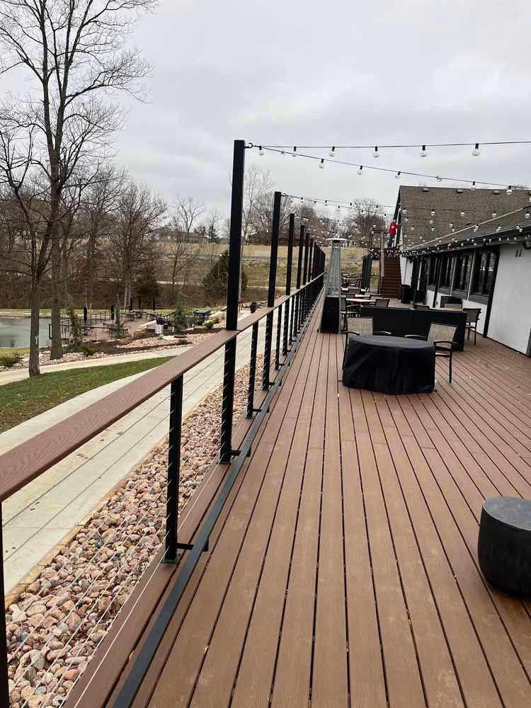 A large wooden deck with a railing and tables and chairs on it.