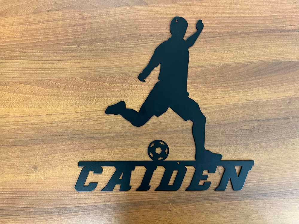 A silhouette of a man kicking a soccer ball with the name caiden on it
