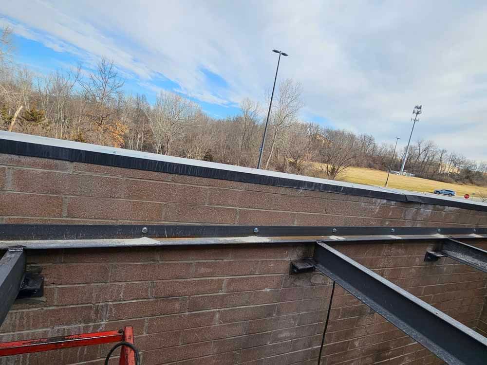 A ladder is sitting on top of a brick wall next to a metal structure.