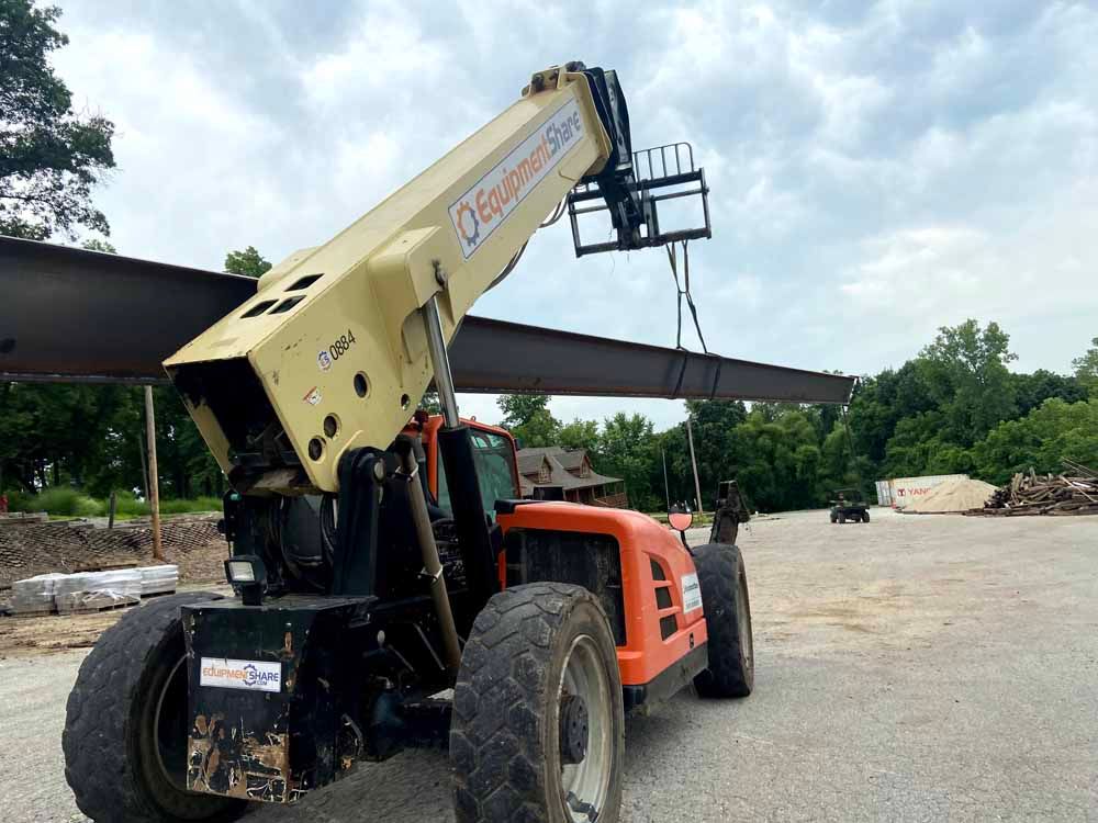A forklift is lifting a large metal beam in a parking lot.