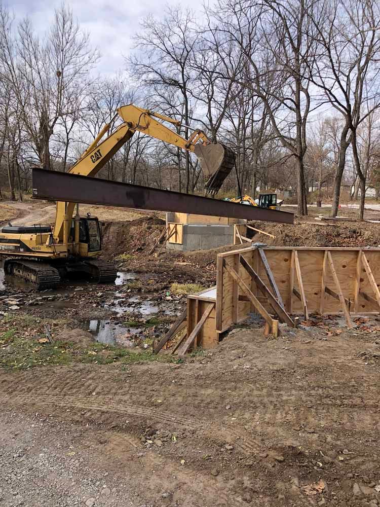 A large excavator is lifting a large metal beam in a dirt field.