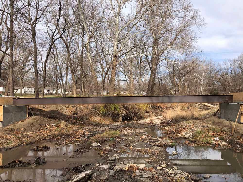 A bridge over a muddy river with trees in the background.