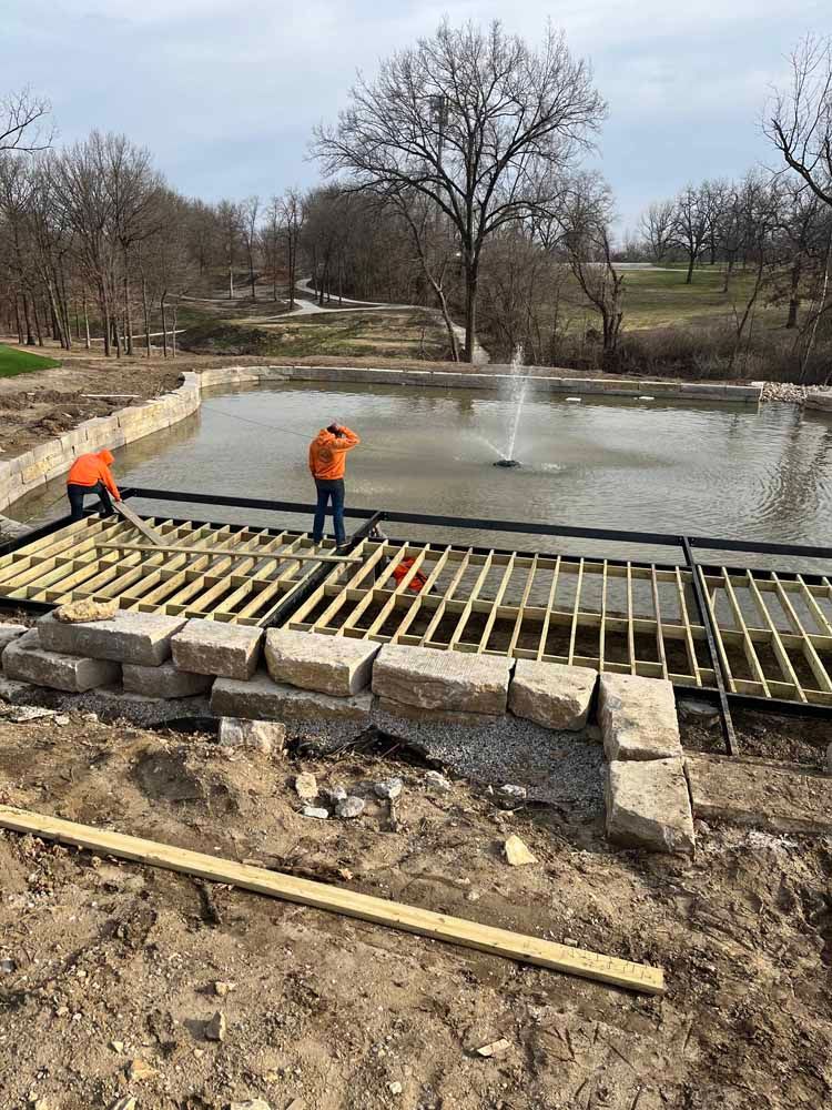 A couple of men are working on a bridge over a pond.