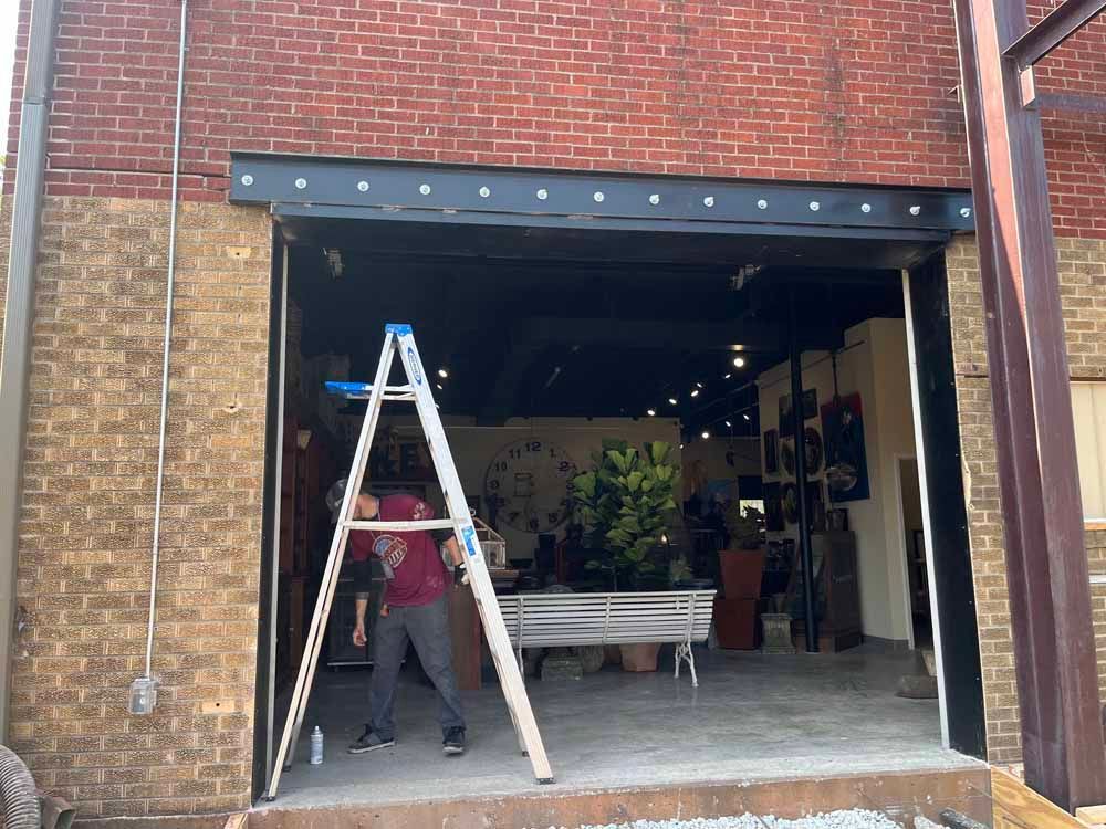 A man is standing next to a ladder in front of a brick building.