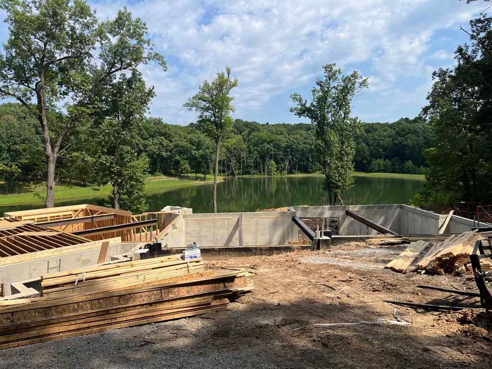 A large concrete wall is being built next to a lake surrounded by trees.