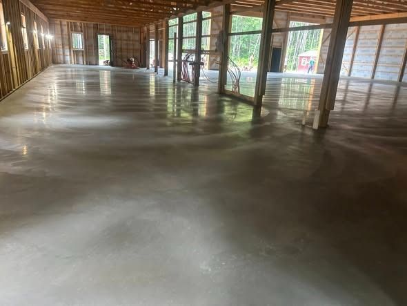Newly poured, polished concrete floor inside a large, unfinished building with wooden framing.