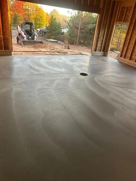 Newly poured concrete garage floor with swirl patterns; construction site exterior visible.