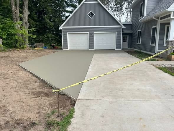 Newly poured concrete driveway next to older concrete section, leading to a gray garage. Yellow caution tape.