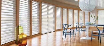 Bright modern dining room with wooden floors, blue chairs, white shutters, and a table by large windows