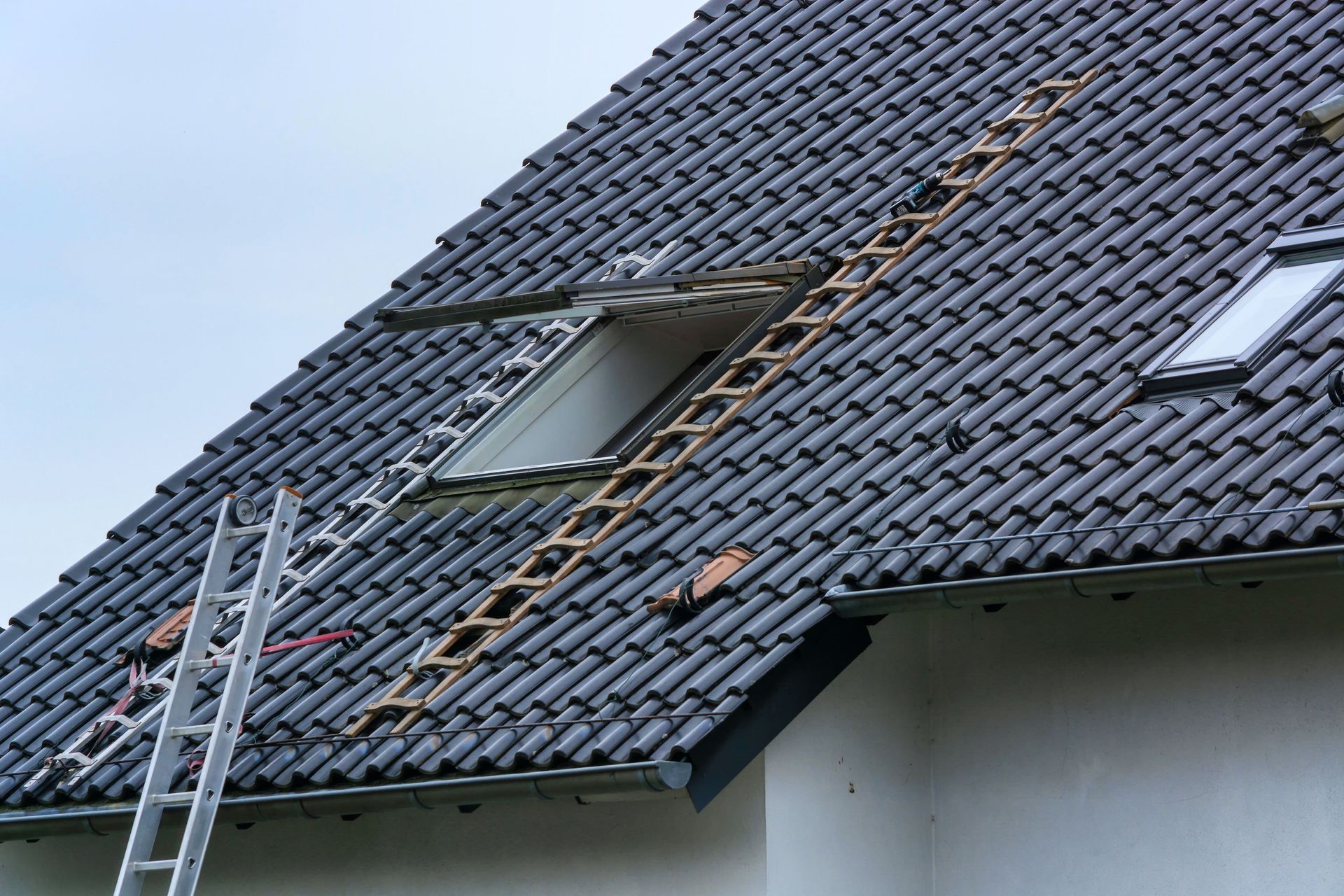 Damaged tiled roof with a ladder and exposed hole after repairs or storm damage
