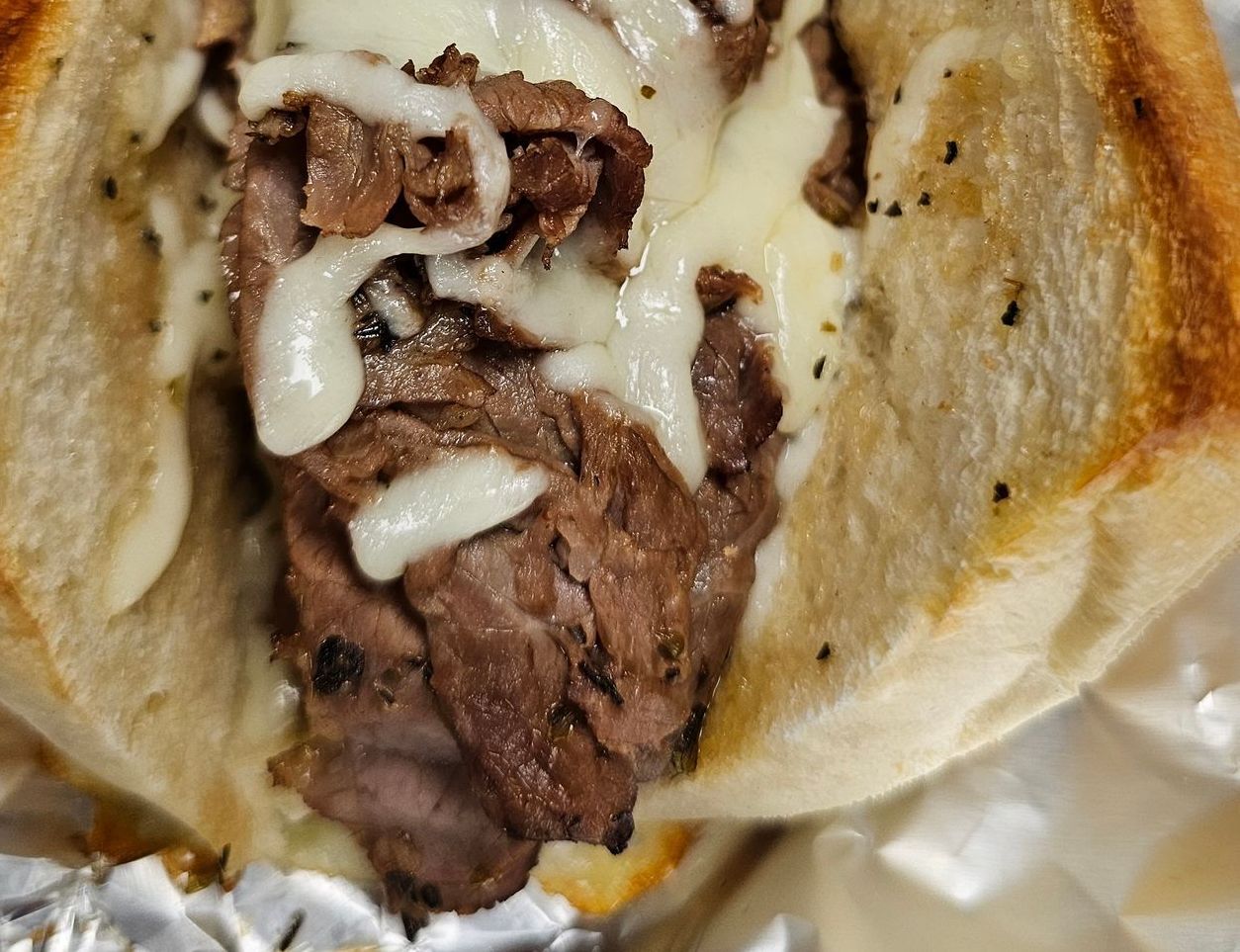 A close up of a steak sandwich wrapped in tin foil.