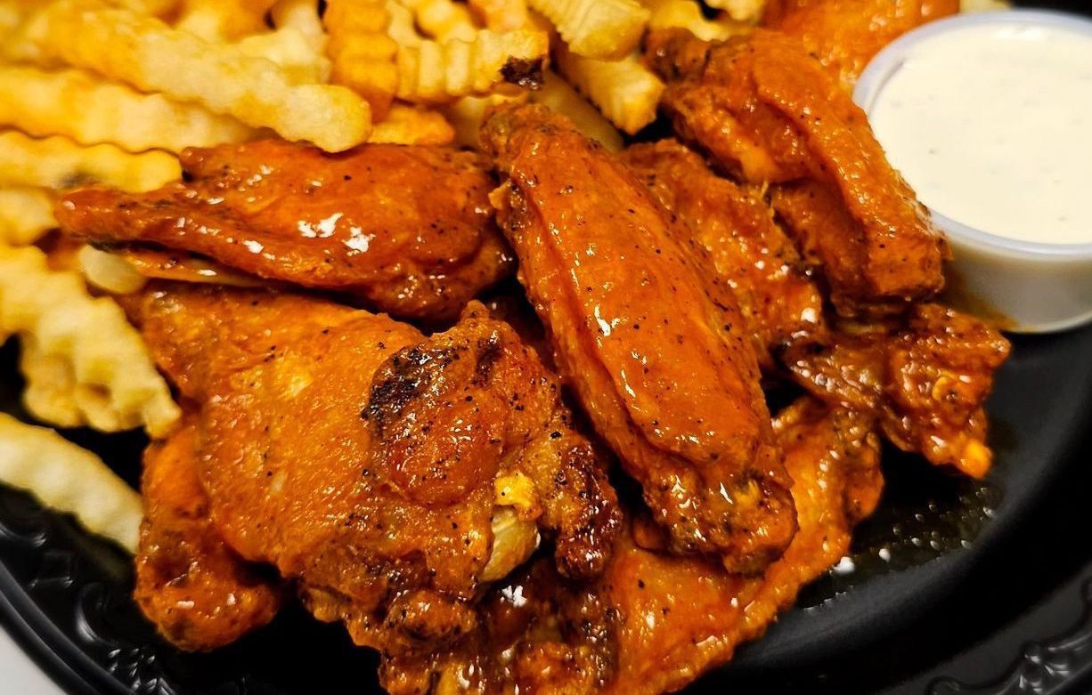 A black plate topped with chicken wings and french fries.