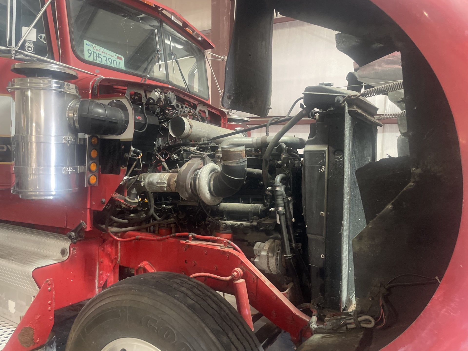 The engine of a red semi truck is being worked on in a garage.