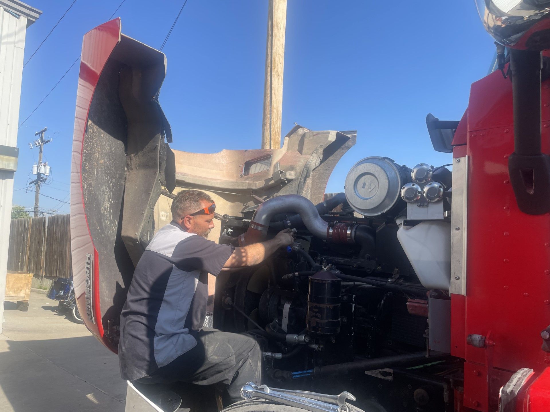 A man is working on the engine of a red truck.