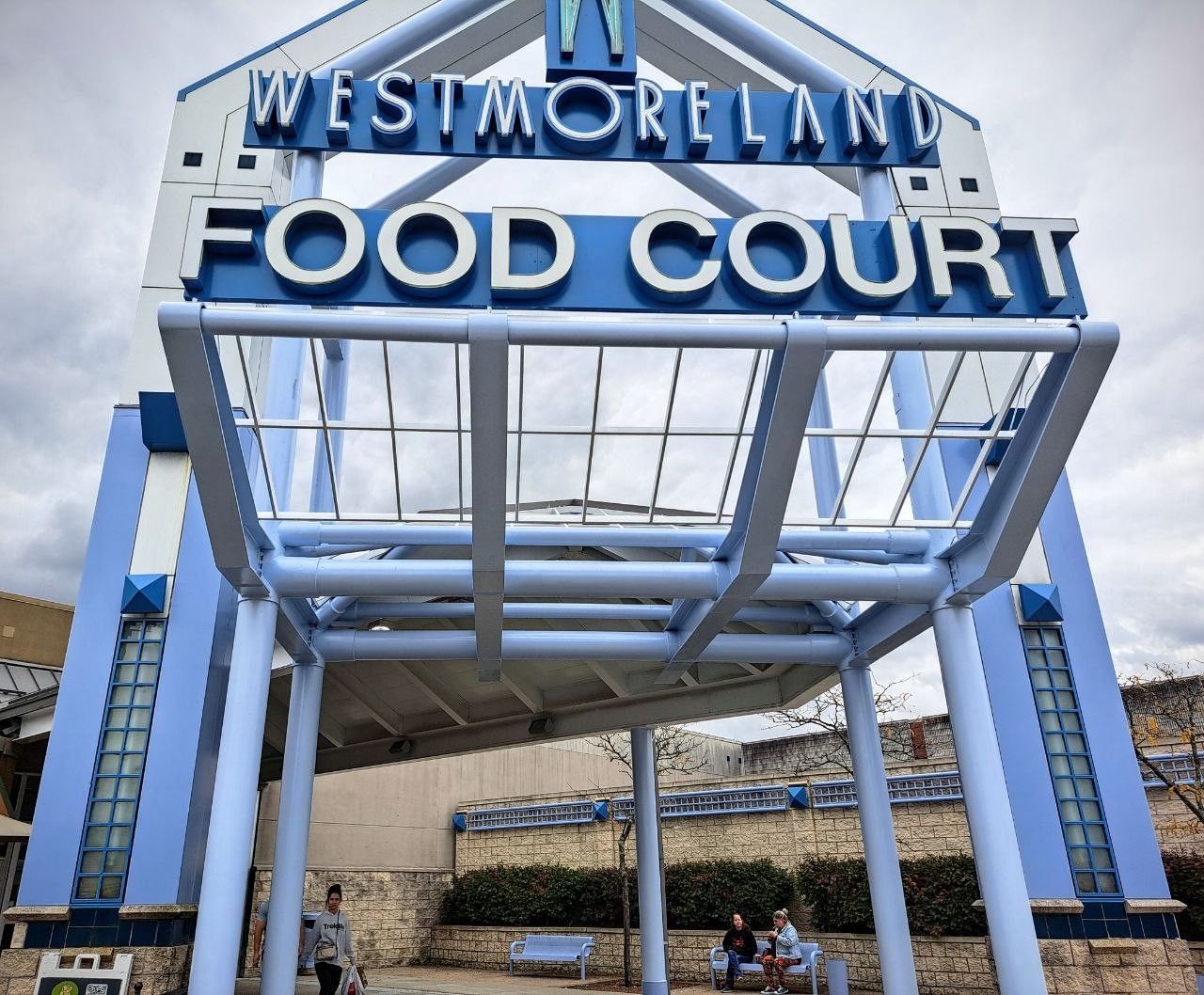 Westmoreland Food Court entrance with blue and white signage. People sit on a bench in front.