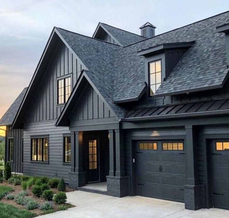 Dark gray house with matching garage doors, black roof, and manicured landscaping.