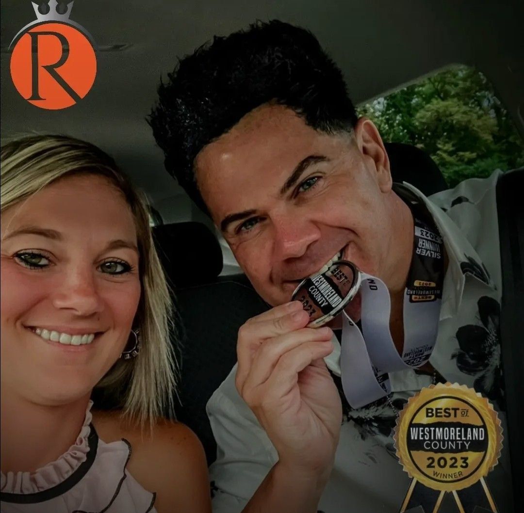 Woman and man smiling, man holding medal. Inside a car.