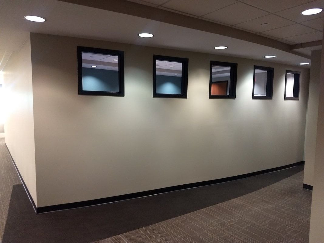 Hallway with tan walls, recessed lighting, and rectangular windows with black frames.