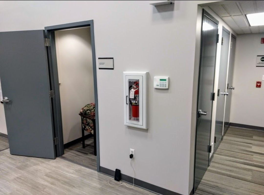 Fire extinguisher in a white cabinet on a gray wall. Open doorway, glass doors, and hallway.