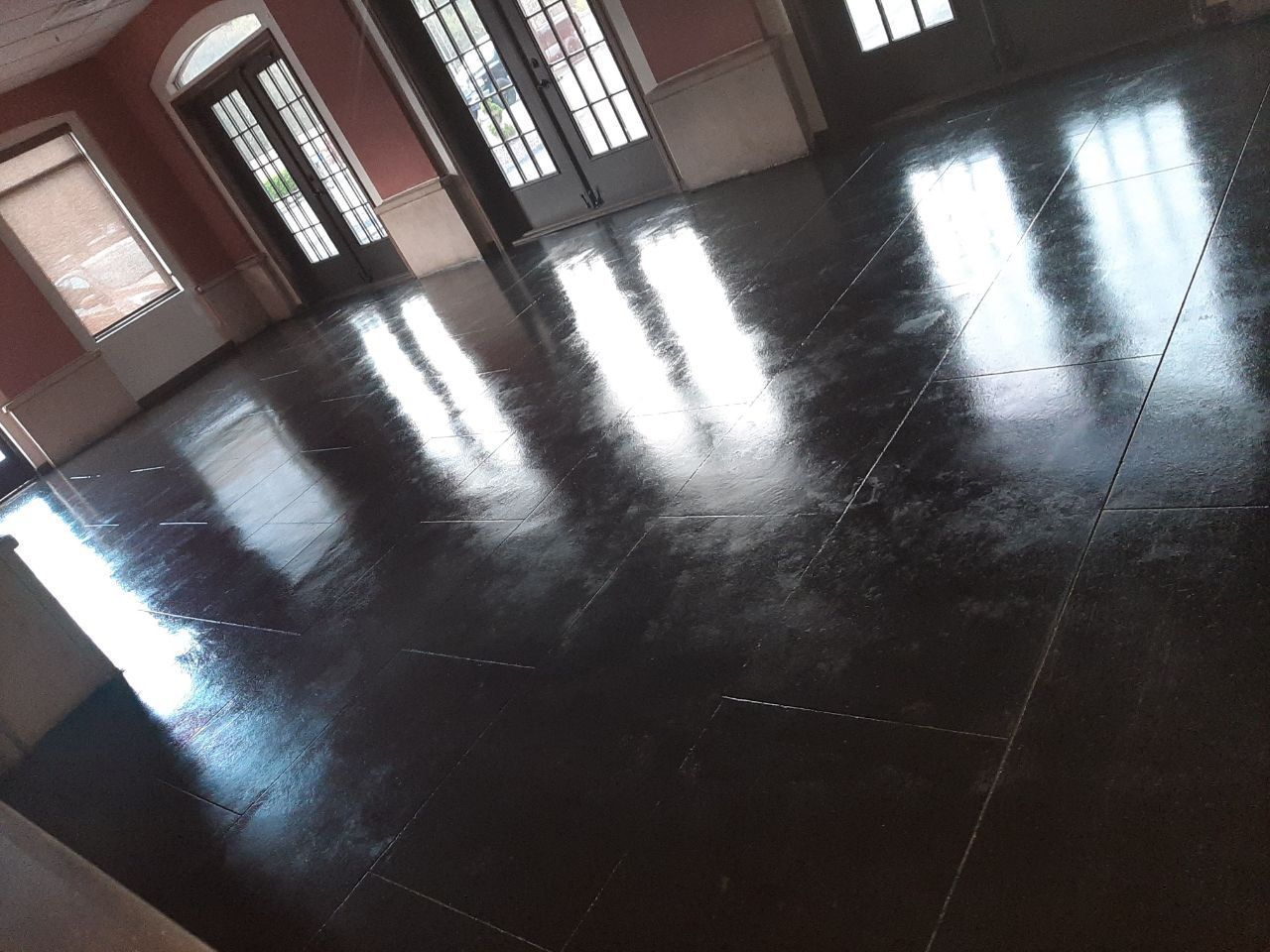 Shiny, dark wooden floor reflecting sunlight from windows in an empty room with light pink walls.