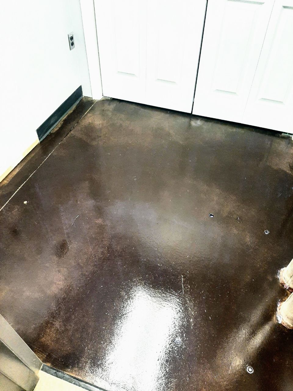 Dark brown stained concrete floor with white splotches near a doorway and wall.