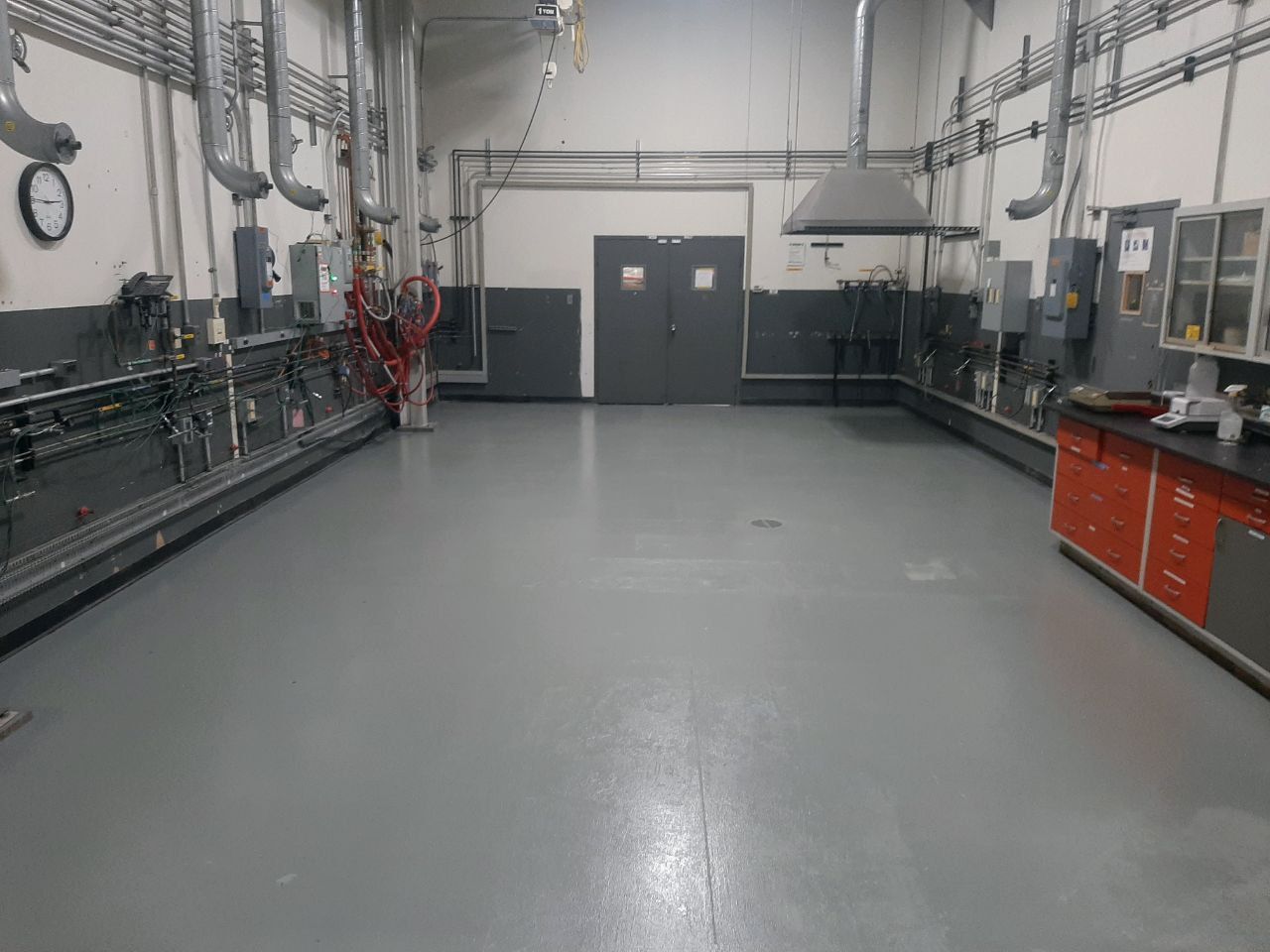 A large industrial room with gray floor and walls, equipment, and a double door.