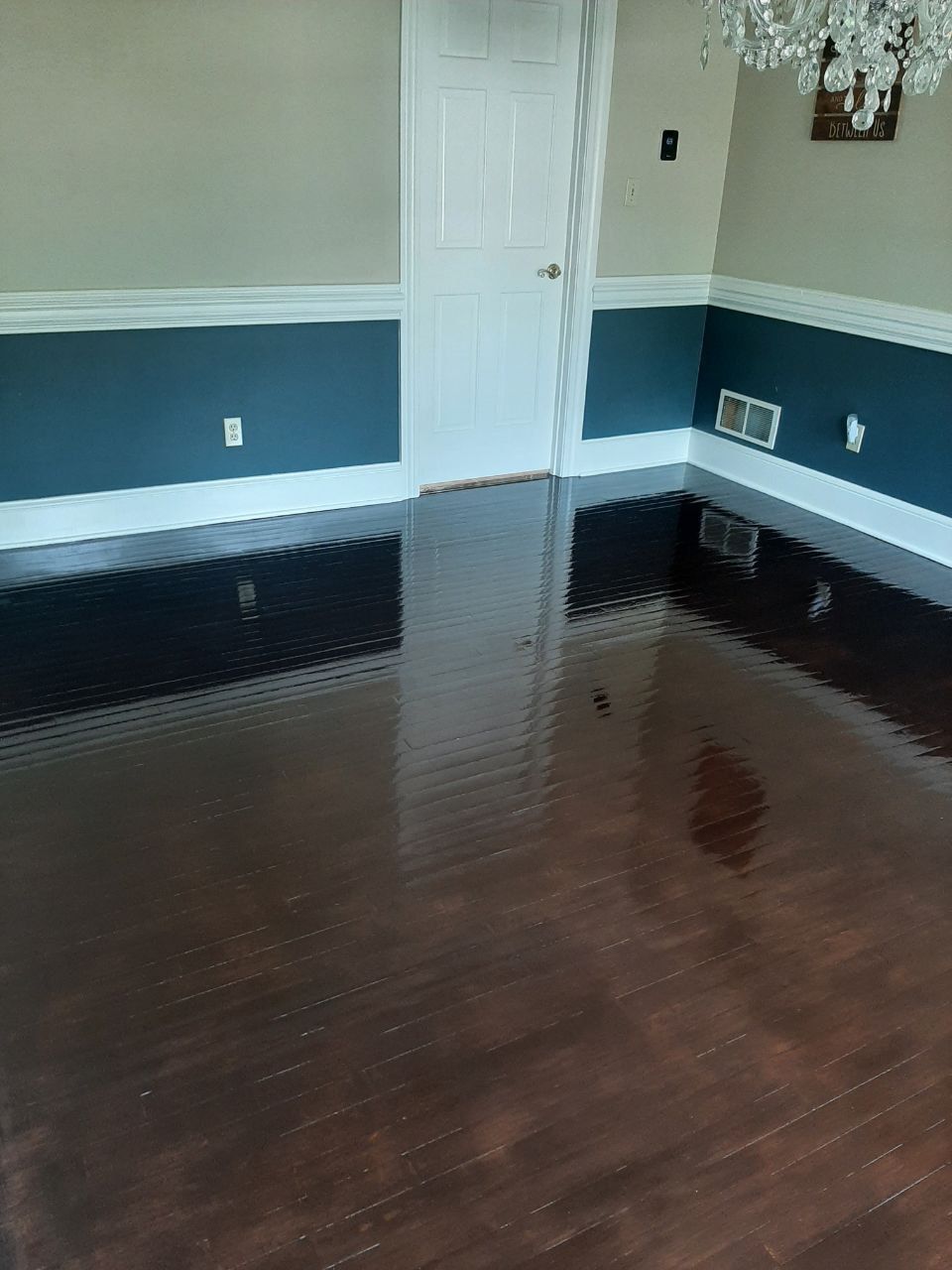 Dark, glossy wood-look floor reflects walls painted blue and white. White door is in the center of the image.