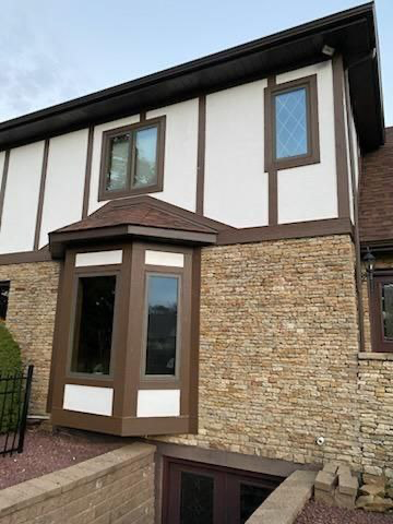 Two-story house with stone and white stucco exterior, brown trim, and a bay window.