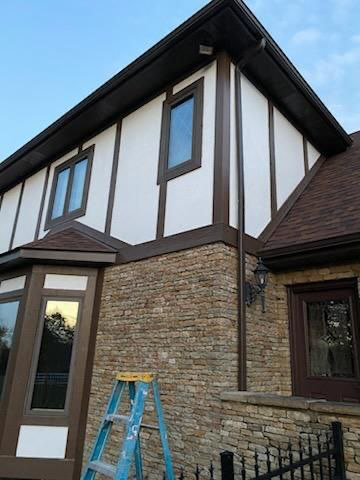 Two-story house with stone and white facade, brown trim and windows, a ladder in front, blue sky.