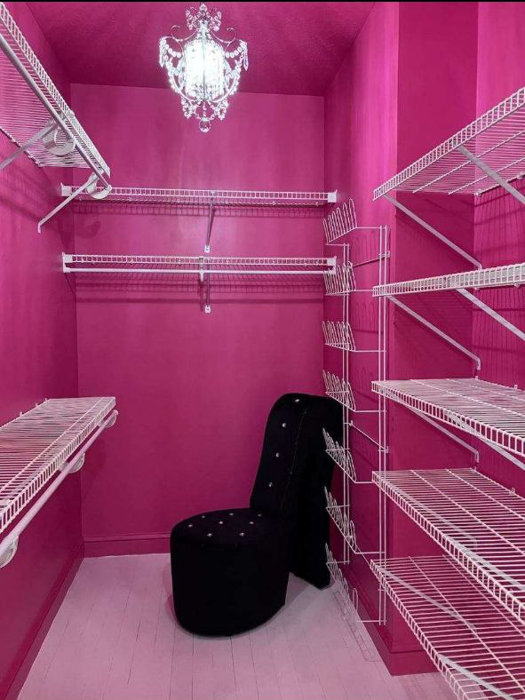Pink walk-in closet with white wire shelving, black chair, and crystal chandelier.