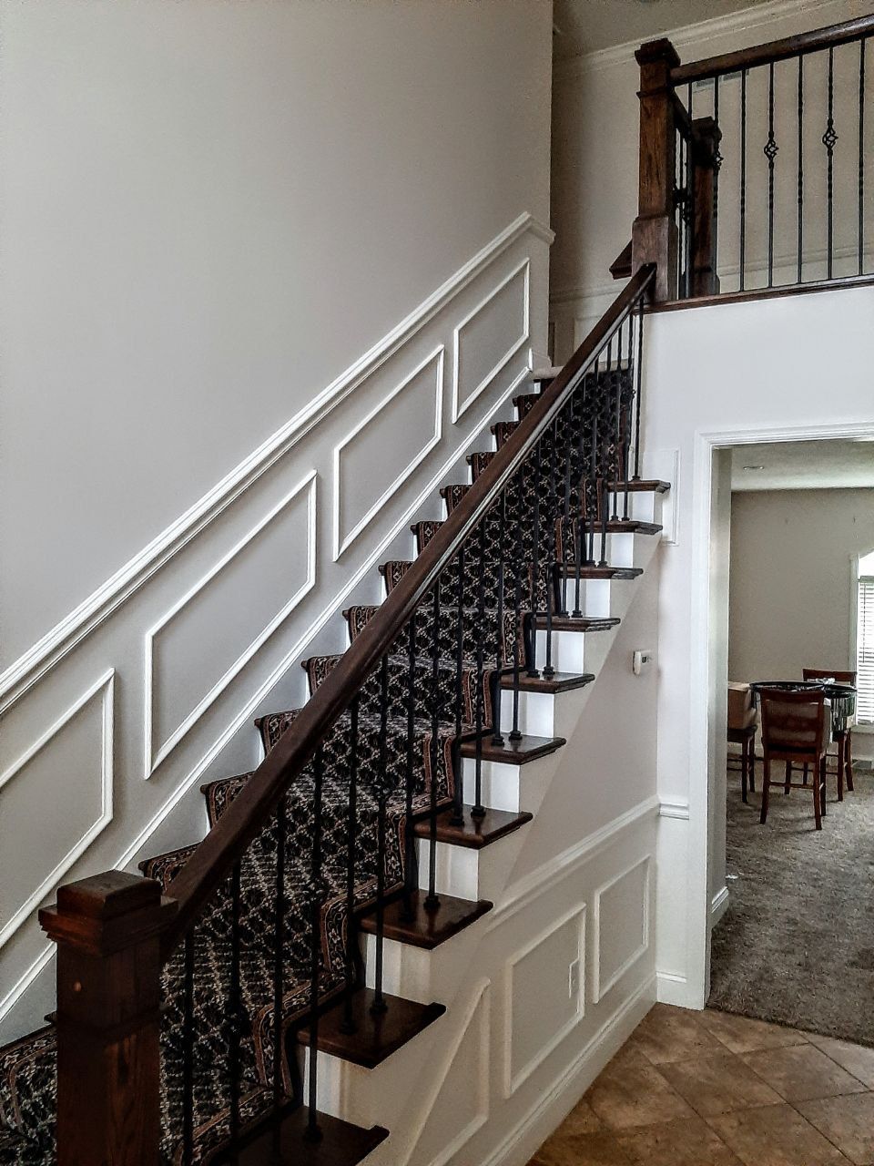 Staircase with dark wood railing and patterned carpet runner, white paneling on the walls.