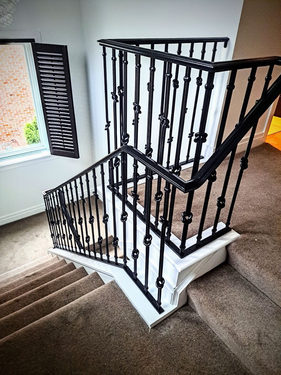 Staircase with black metal railings, white trim, and carpeted stairs. A window with shutters is visible.