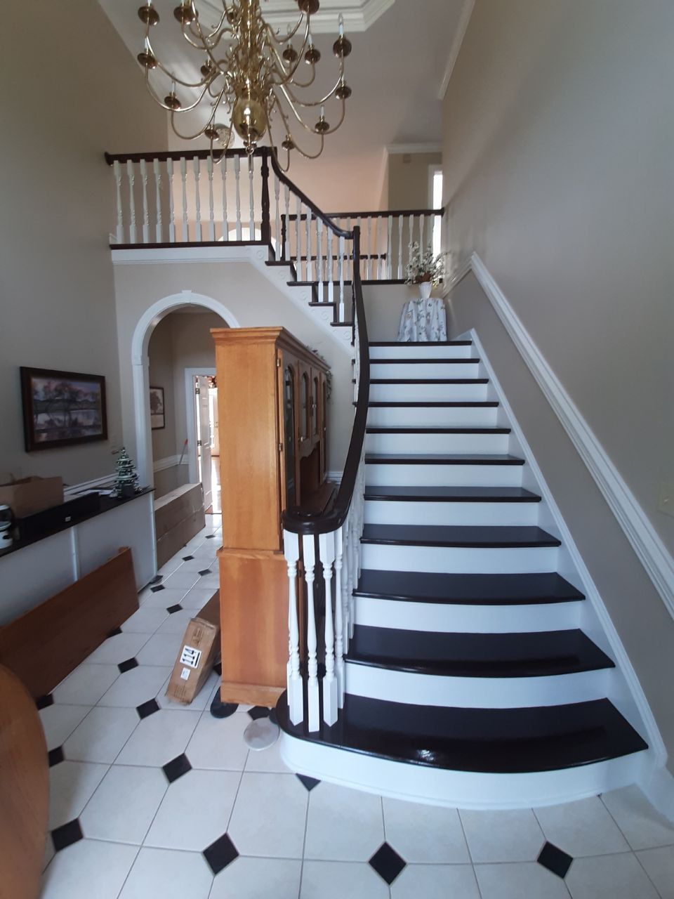Entryway with a staircase, white and black steps, ornate chandelier, and white railing.